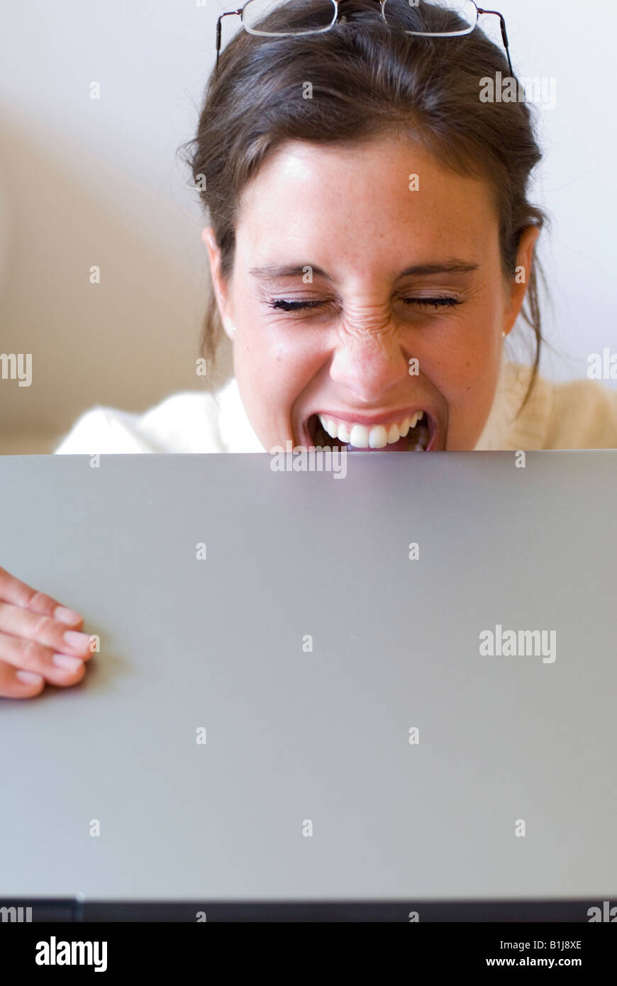 Giovane donna di mordere sul suo computer portatile in frustrazione Foto Stock