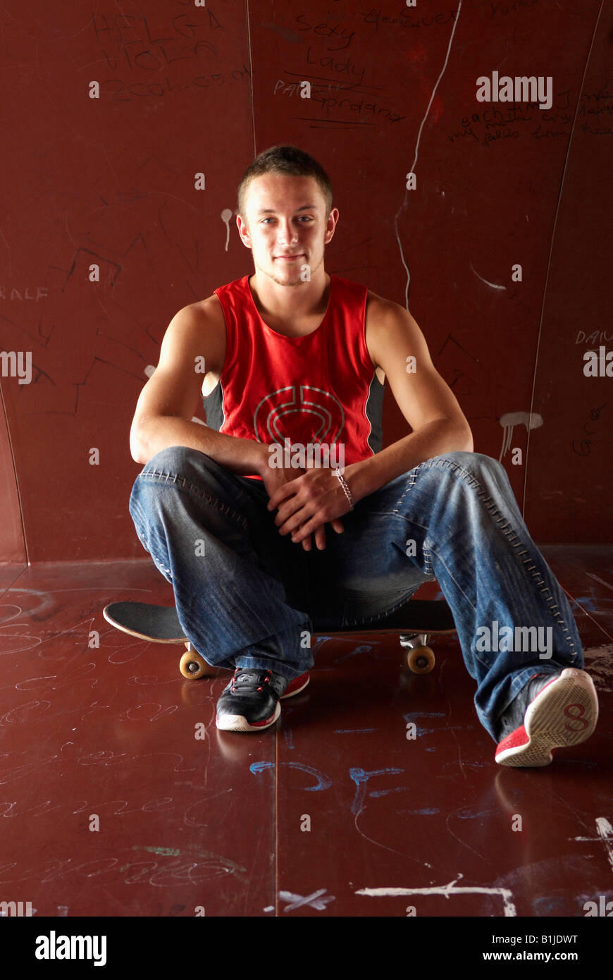 Adolescente di sesso maschile seduto sul suo skateboard Foto Stock