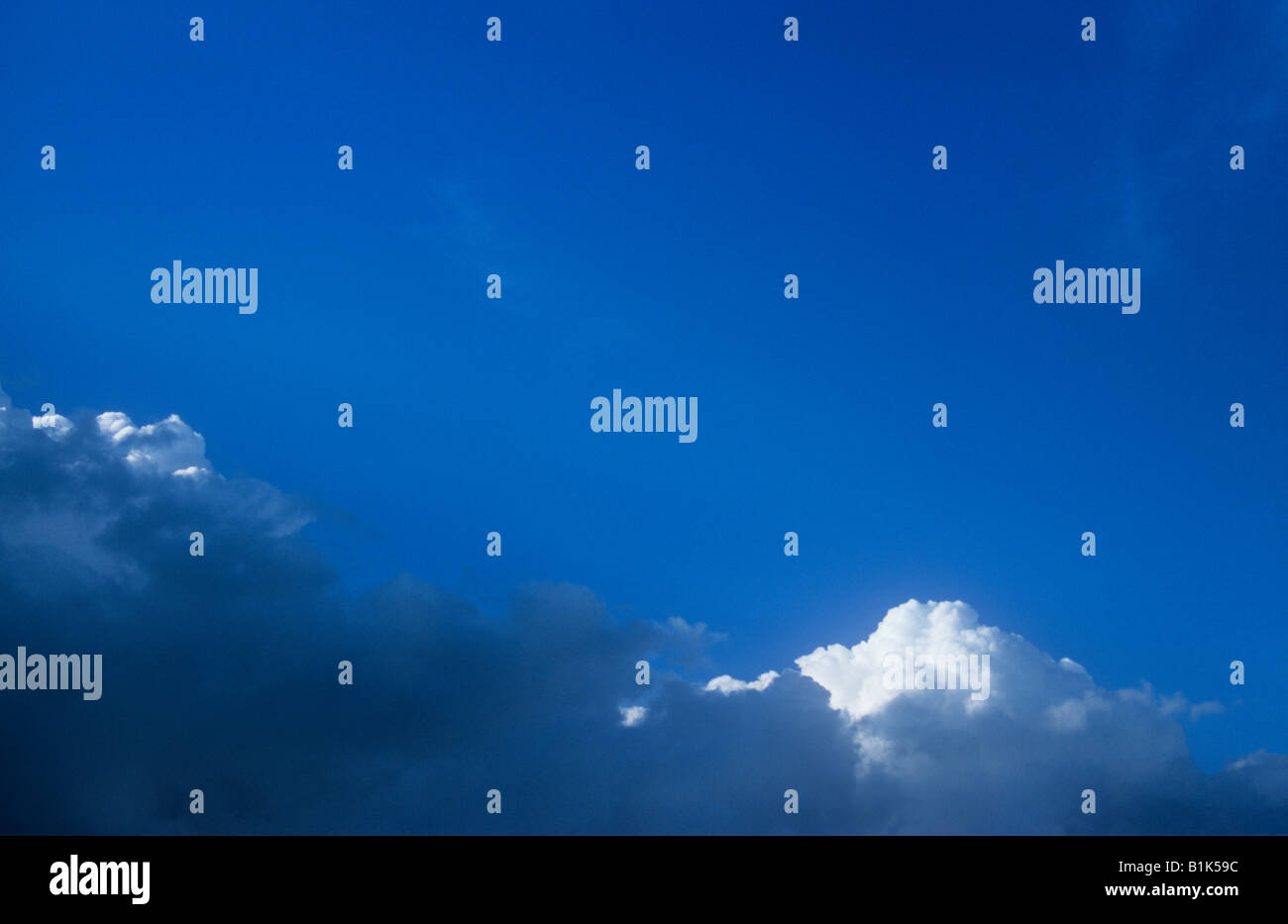 Il bianco e il grigio nuvole temporalesche raccolta e ondeggianti al di sotto di una vasta distesa di cielo blu chiaro Foto Stock