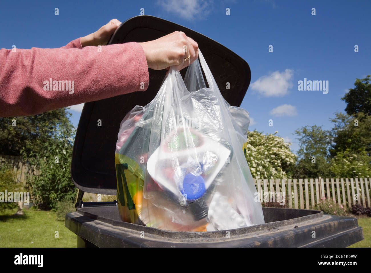 Donna mettendo il sacchetto in plastica dei rifiuti domestici in nero bidone con ruote per buttare fuori. Inghilterra Regno Unito Gran Bretagna Foto Stock