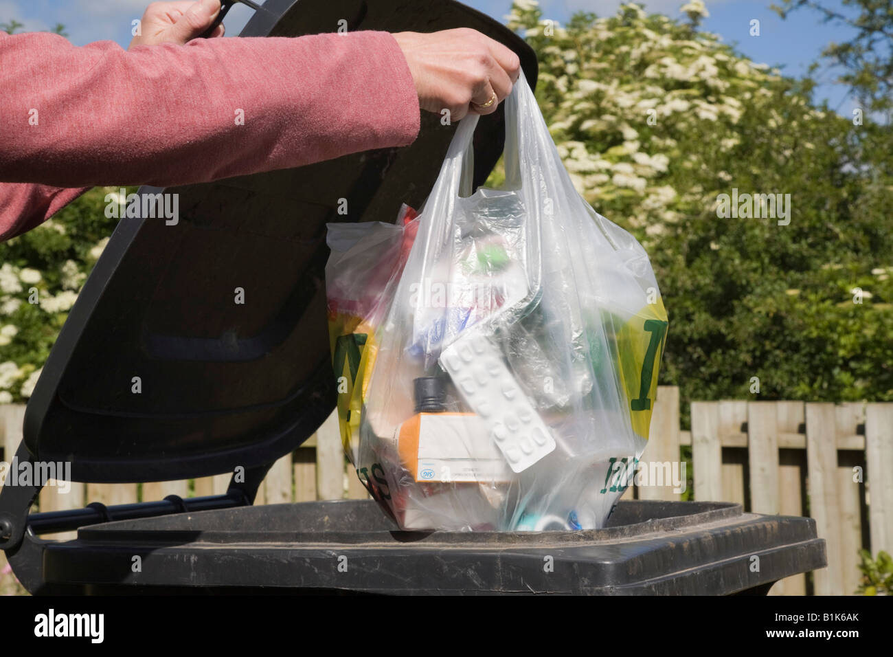 Donna mettendo il sacchetto in plastica dei rifiuti domestici in nero bidone con ruote per buttare fuori. La Gran Bretagna REGNO UNITO Foto Stock