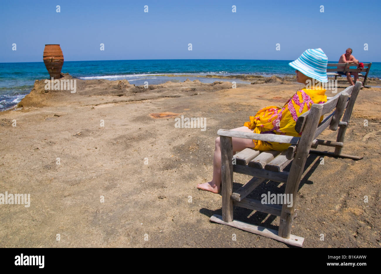 Due persone sedersi sul banco vicino a grandi urna cretese sulla spiaggia di Malia sul Greco isola mediterranea di Creta Foto Stock