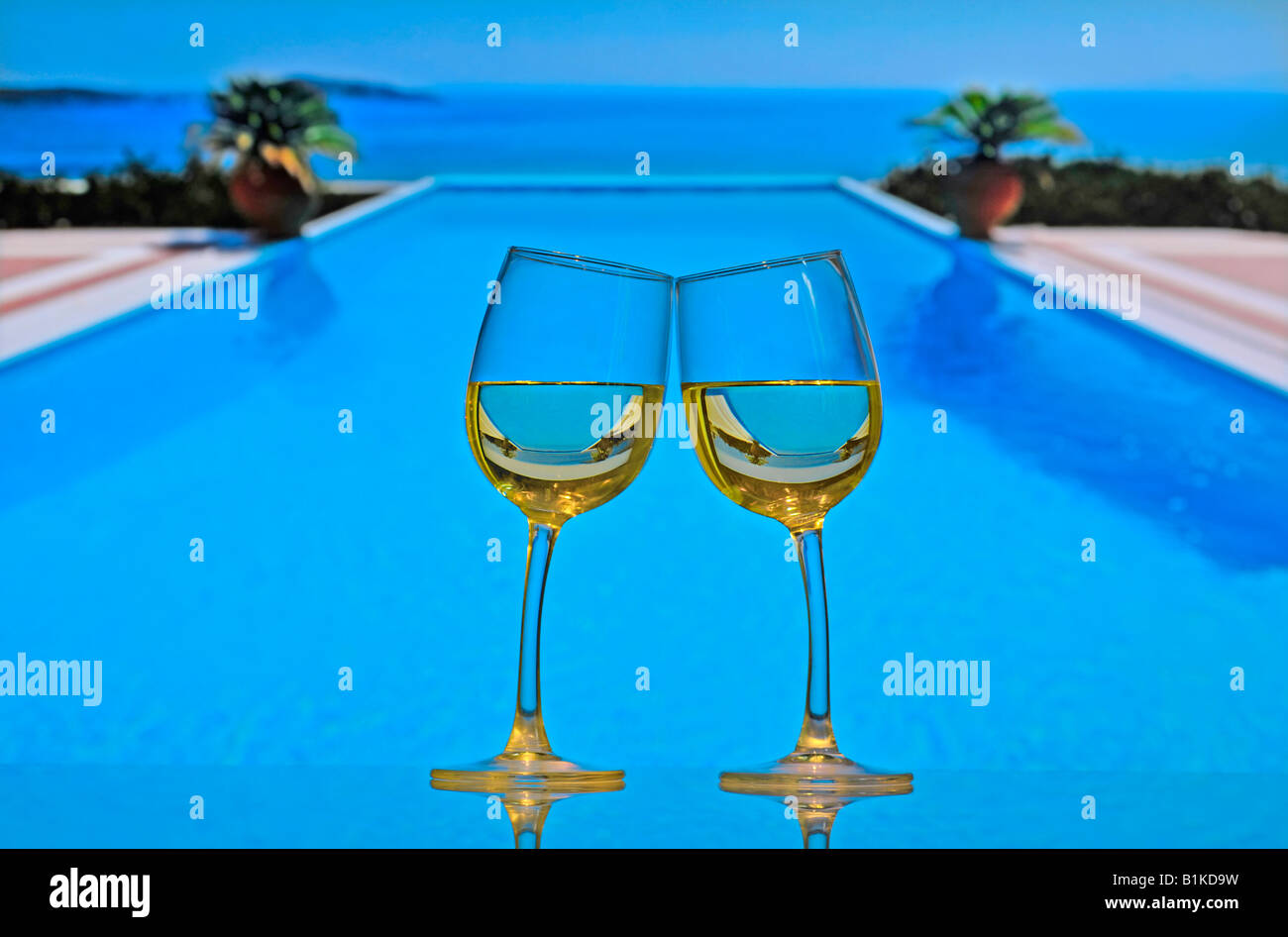 Due calici da bianco sul tavolo lean gli uni verso gli altri e 'spiraglio', con piscina infinity e mare in background Foto Stock