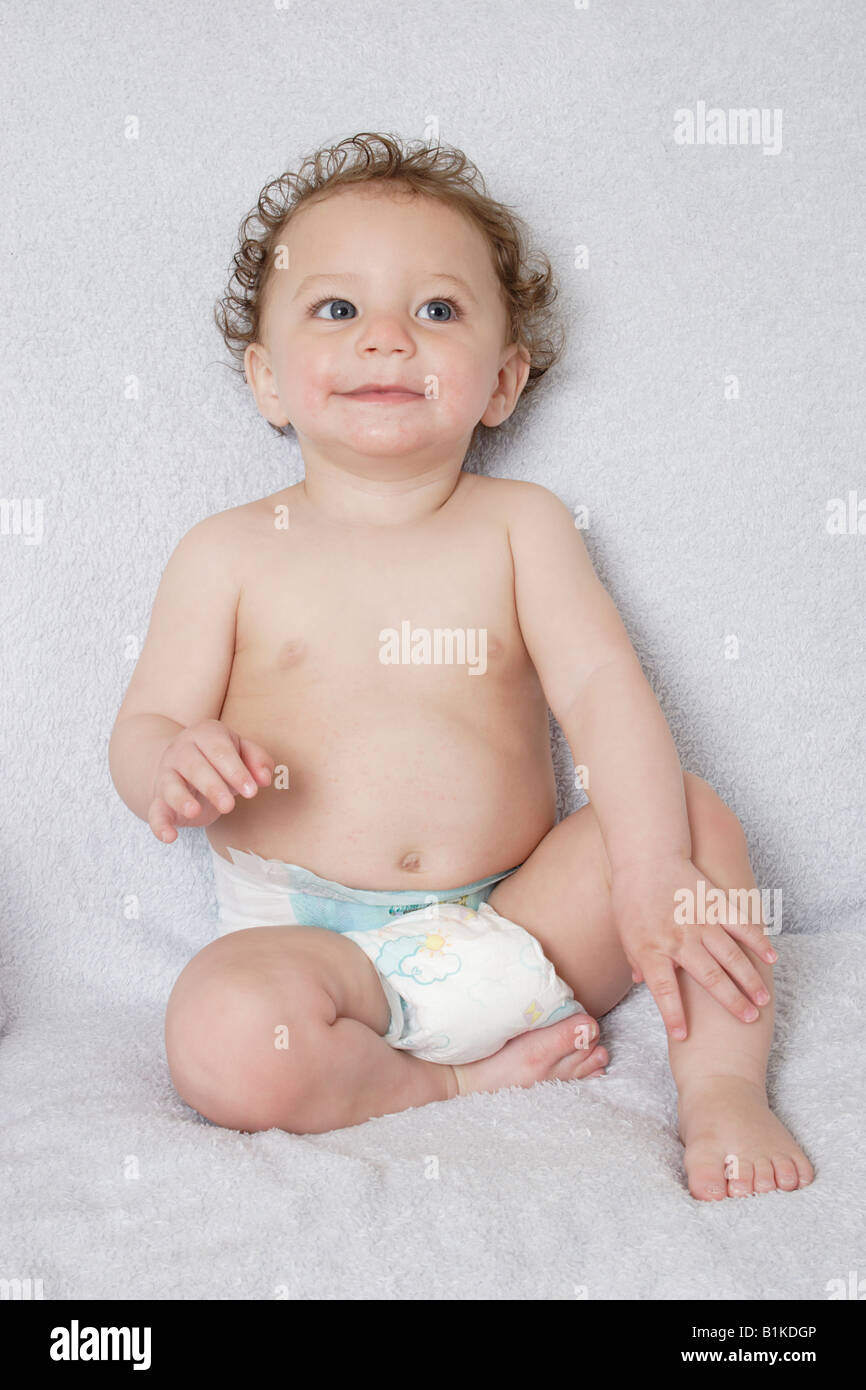 Ritratto piccolo bambino di età compresa tra i sette e i dieci mesi nel pannolino monouso nudo seduto Foto Stock