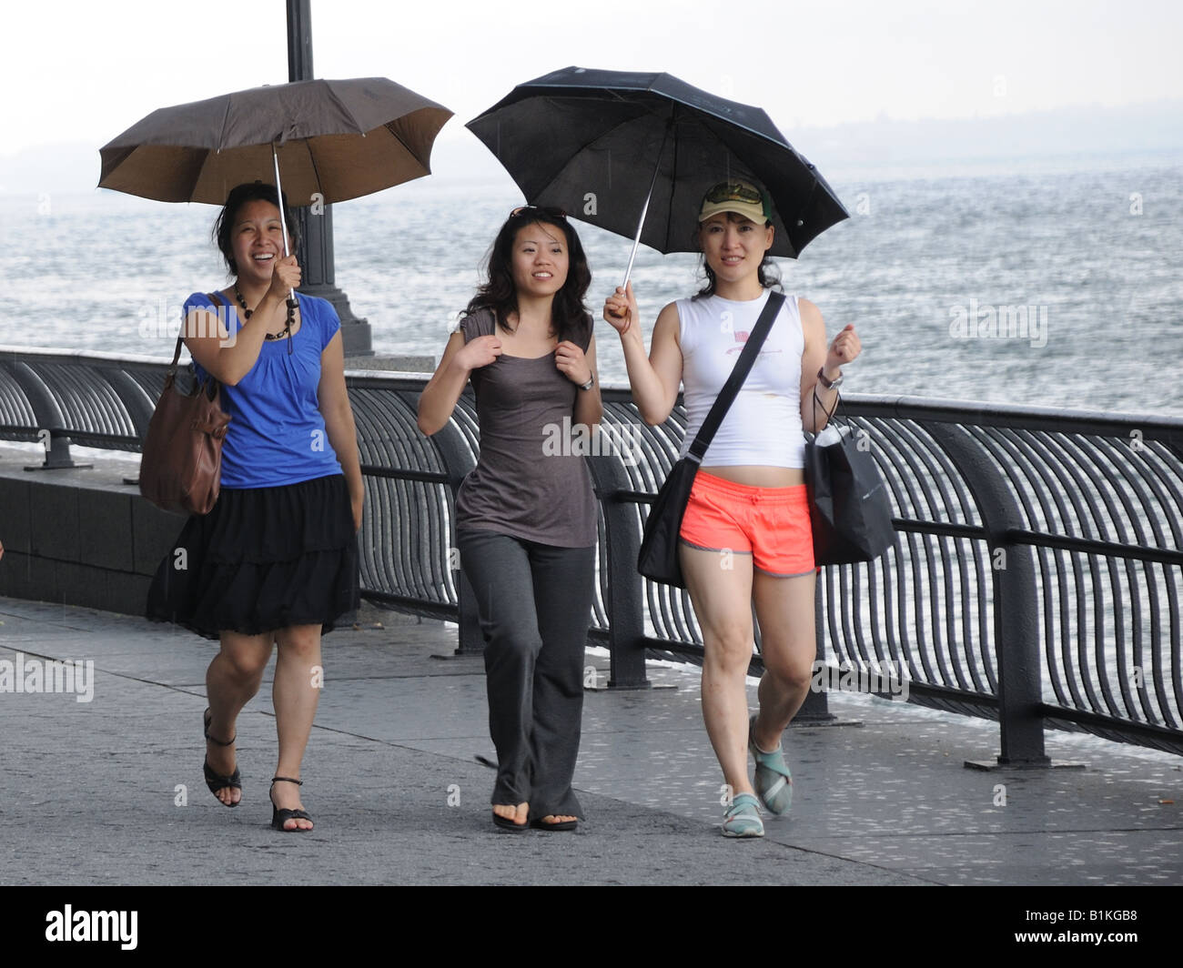 Tre giovani donne a piedi lungo il Battery Park City esplanade sotto la pioggia. Foto Stock