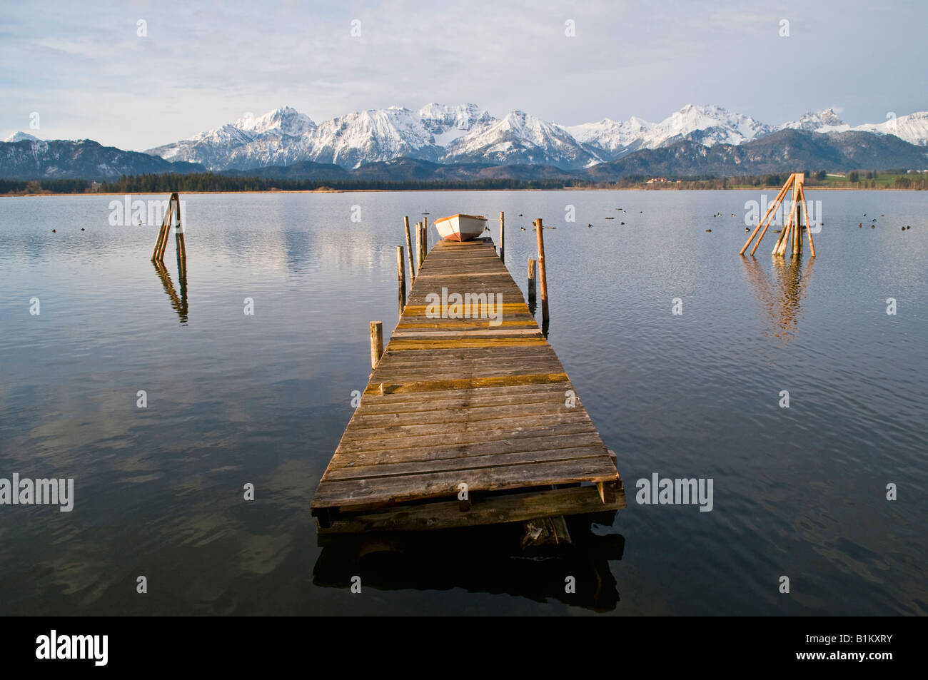 Piccolo canotto sul dock di legno in Hopfensee con montagne coperte di neve in background Baviera Germania Foto Stock