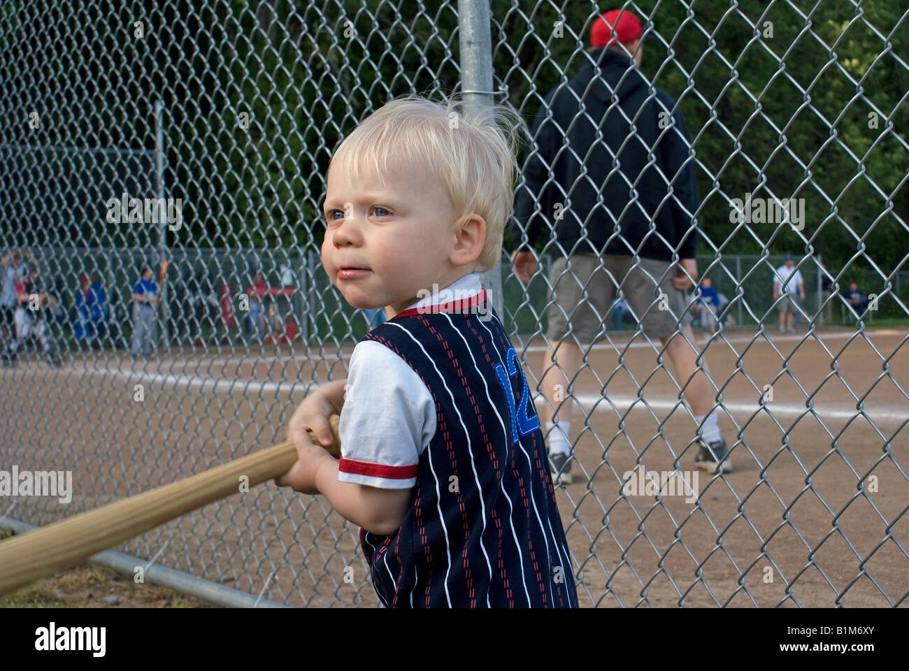 Il Toddler oscillazione un bat mentre guardi i suoi fratelli giocare a baseball. Foto Stock