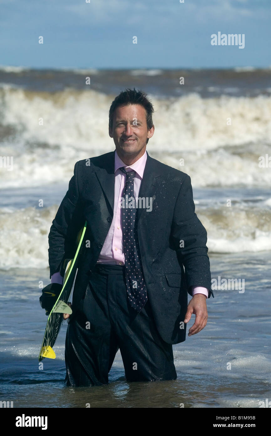 Un uomo d'affari nel suo business suit in acqua holding di una tavola da surf Foto Stock