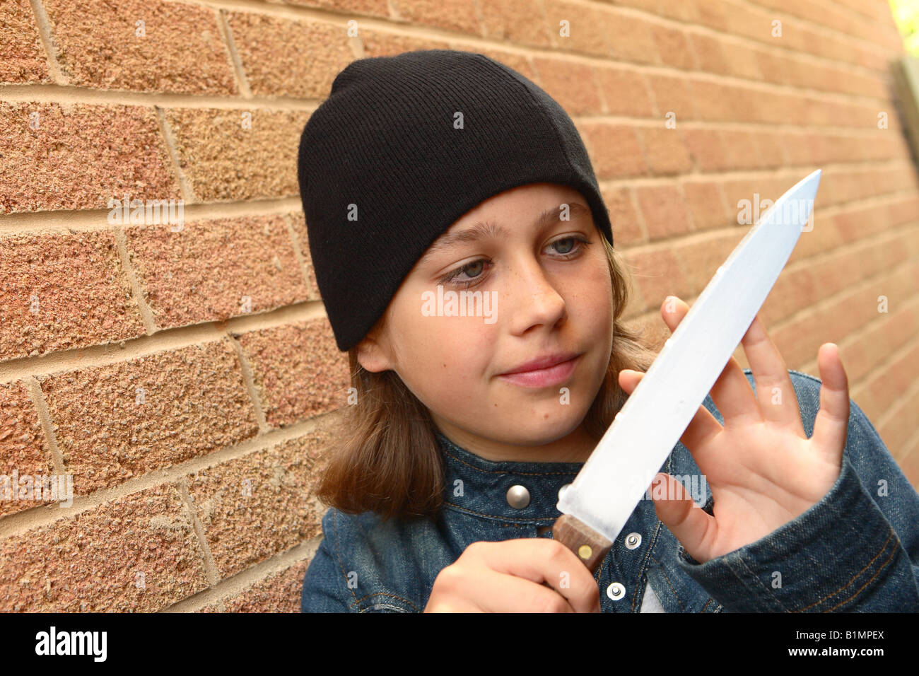 Giovane ragazza adolescente con coltello affilato camicia denim piano di tracciatura della vendetta in strada urbana alley con muro di mattoni posti dal modello Foto Stock