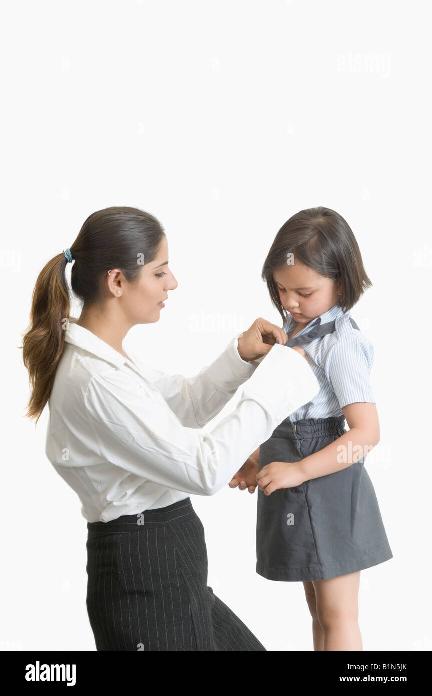 Profilo laterale di una giovane donna di aiutare la propria figlia in indossano uniformi scolastiche Foto Stock