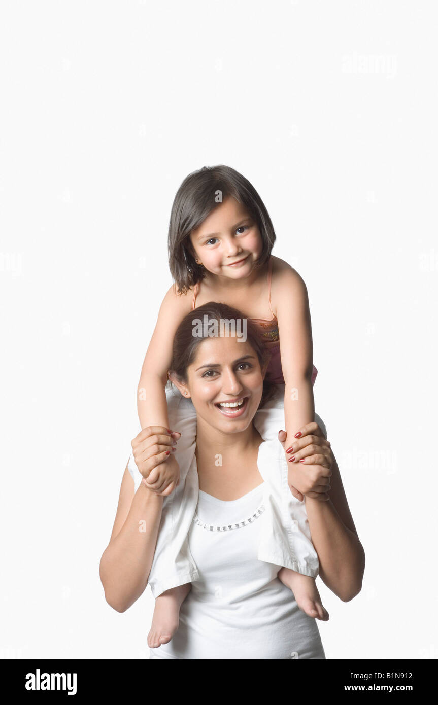 Ritratto di una giovane donna che porta la figlia sulle sue spalle e sorridente Foto Stock