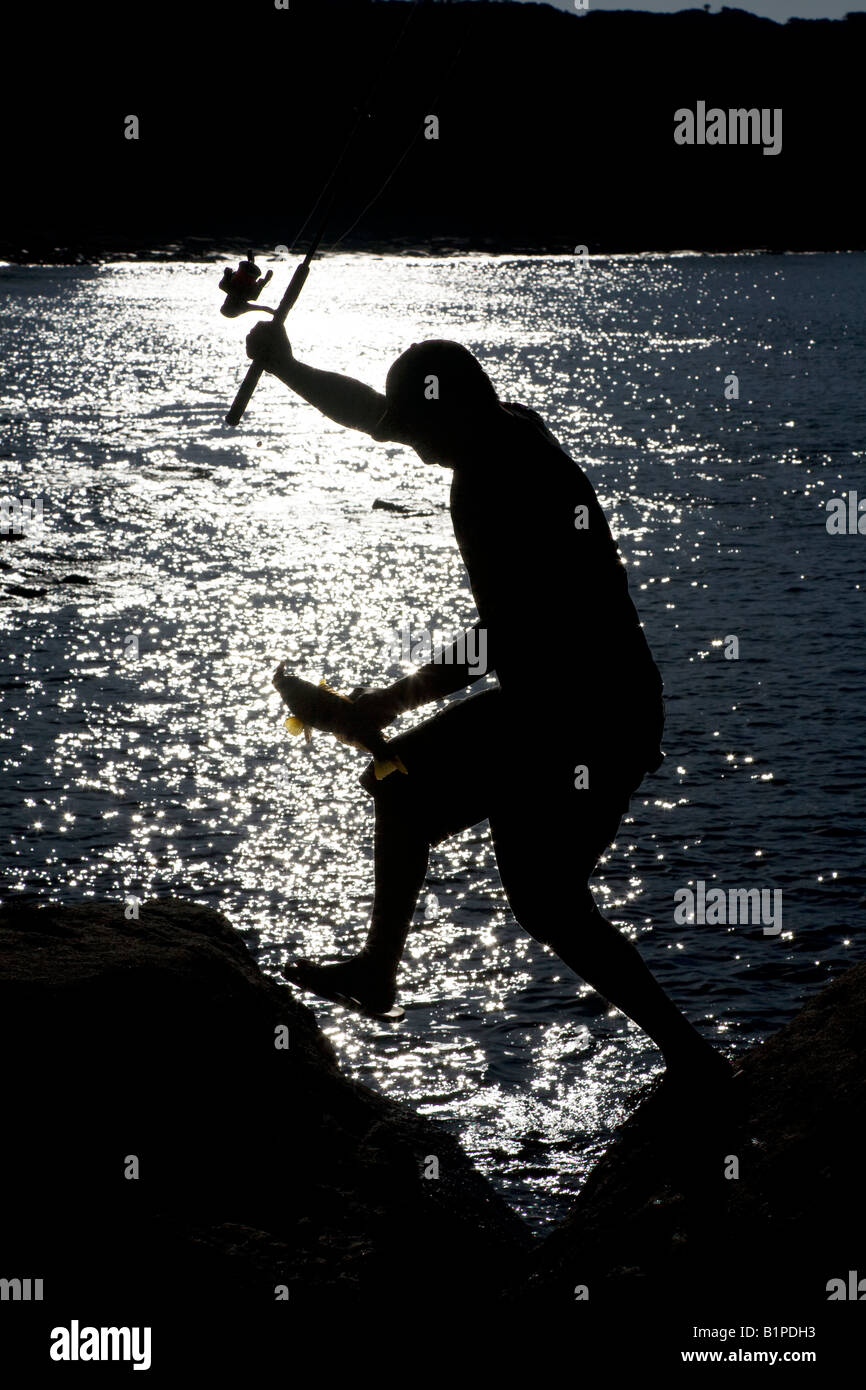 Un pescatore passa attraverso le rocce con un pesce in mano, stagliano contro l'acqua Foto Stock