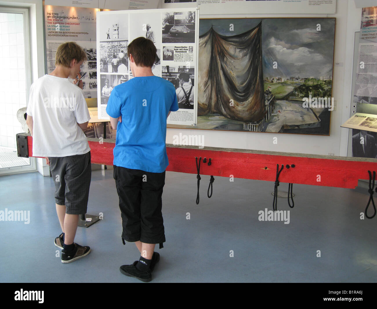 I giovani visitatori guardando le foto correlate di successo i tentativi di fuga dalla Germania Est presso il privato Checkpoint Charlie Berlino Germania Foto Stock