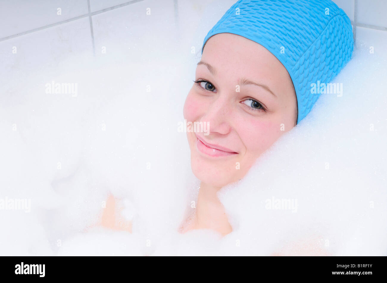 Piuttosto giovane donna tenendo bagno nella vasca da bagno e rilassante, blu della cuffia Foto Stock