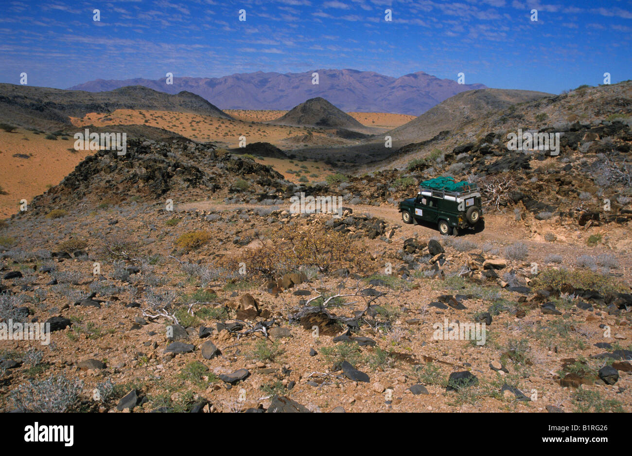 Land Rover nel deserto pietroso paesaggio, Brandberg sfondo di montagne, vicino Uis, Namibia, Africa Foto Stock