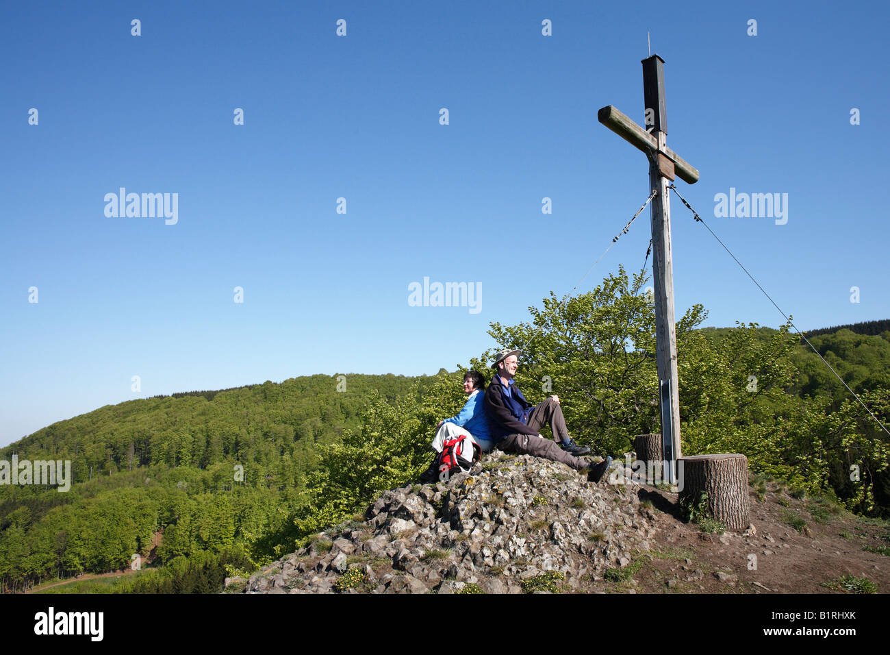 Giovane seduto sotto una croce di vetta del Monte Rockenstein vicino Bischofsheim-Oberweissenbrunn, Hohe Rhon montagne, inferiore Foto Stock