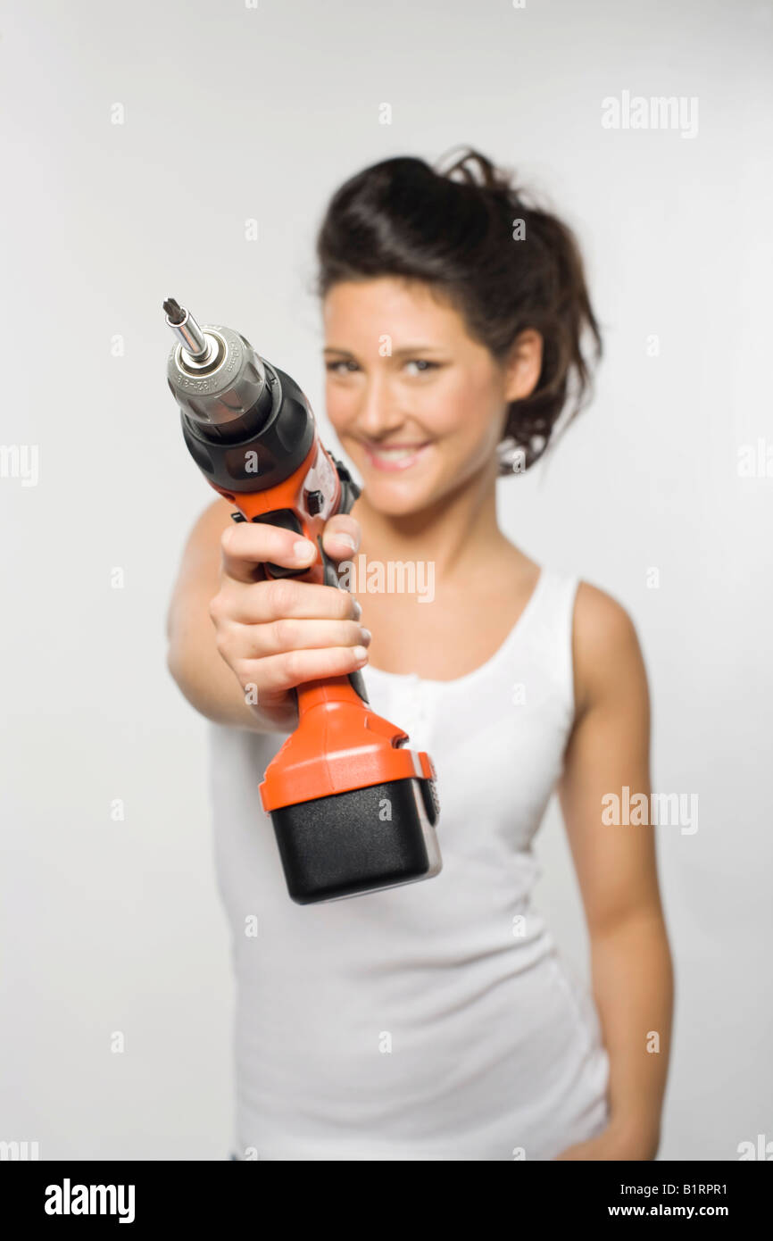 Giovane donna sorridente mentre tiene un trapano elettrico verso la telecamera Foto Stock