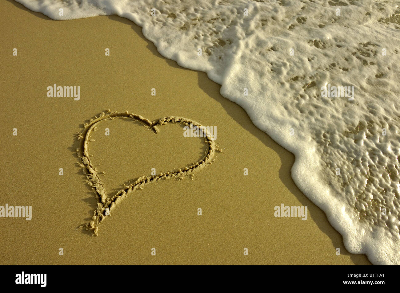 Un cuore disegnato nella sabbia in procinto di essere lavato via da un'onda. Prese in condizioni di scarsa illuminazione di sera. Foto Stock