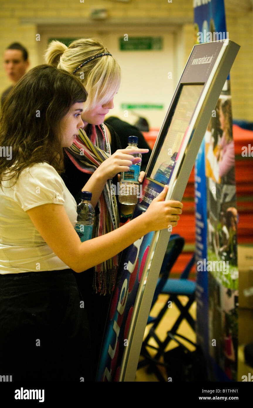 Due sesta forma ragazze accesso alle informazioni sui corsi universitari tramite un touch screen terminale di computer presso la fiera di educazione, Galles Foto Stock