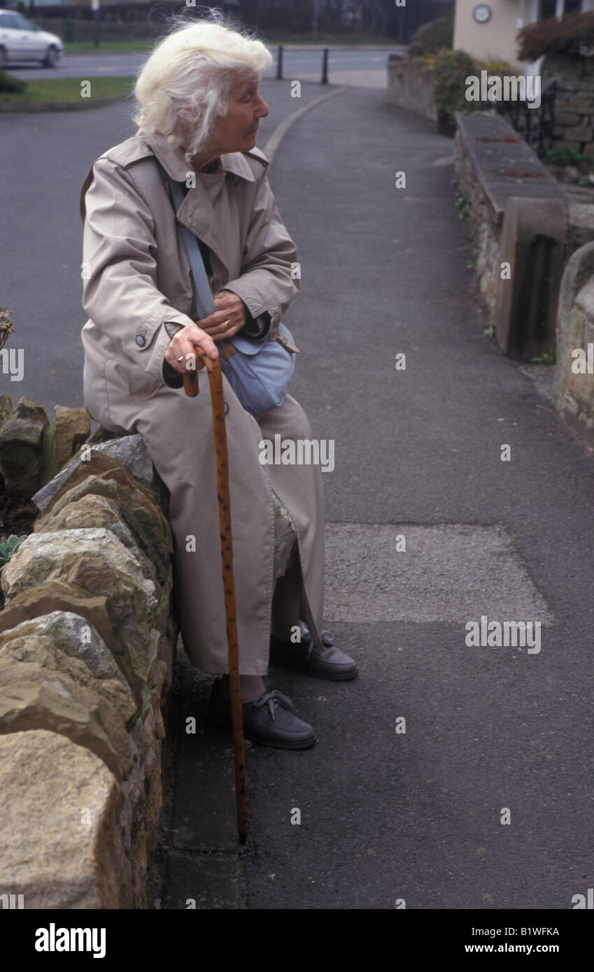 Signora anziana seduti in appoggio contro la parete in strada Foto Stock