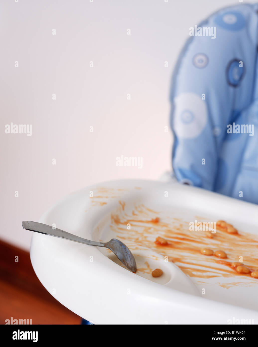 Confuso Childs seggiolone con cucchiaio e fagioli cotti sul vassoio Foto Stock