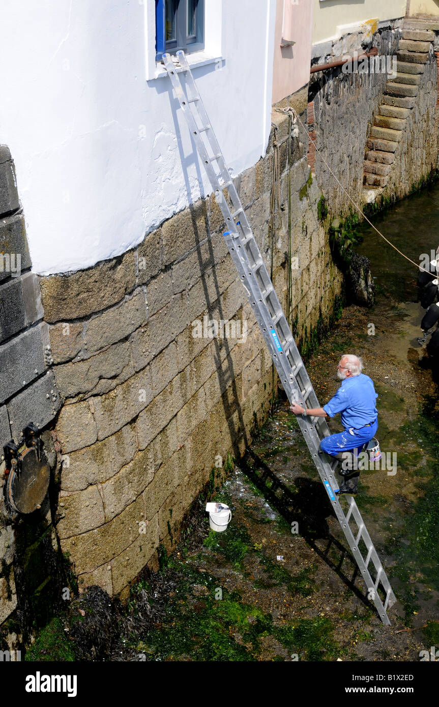 Un pittore su una scala in un porto come la marea entra in Foto Stock