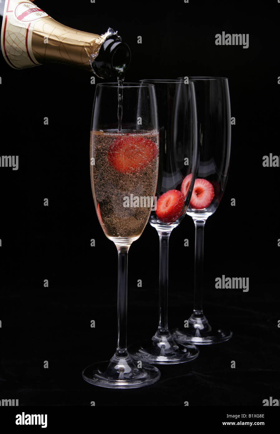 Lo champagne che viene versato in un bicchiere con fragole su sfondo nero Foto Stock