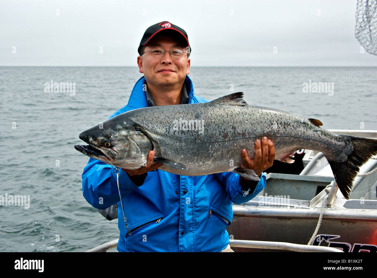 Oriental fisherman tenendo un grande BC Salmone Chinook pesce pescato troll pesca con un grosso cucchiaio esca Foto Stock