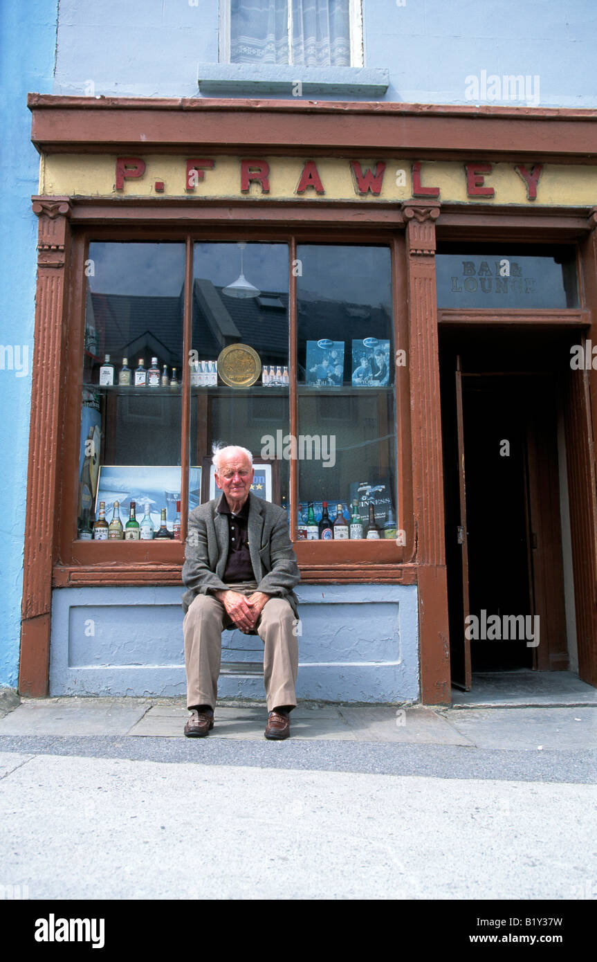 Lahinch village, West Clare, County Clare, old bar pub proprietario si siede davanti al suo pub in un villaggio rurale dell' Irlanda occidentale Foto Stock