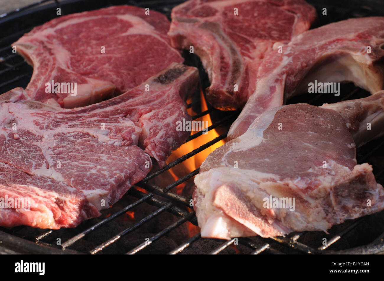 Bistecche e costolette di vitello sfrigolante sulla griglia di un barbecue a carbone. Una leggera fiamma lambisce in fondo alla carne. Foto Stock