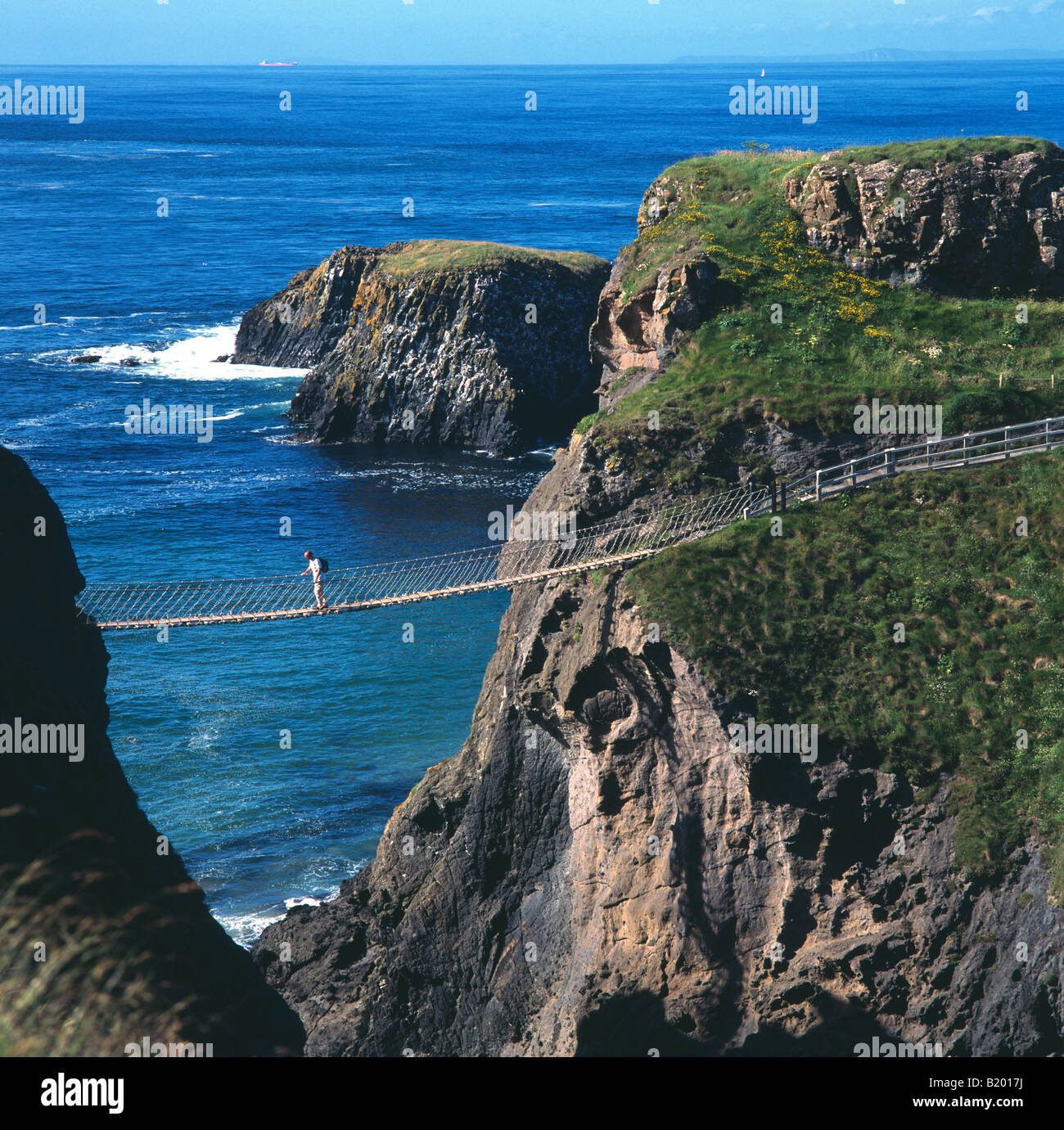 Figura singola traversata Carrick-a-Rede ponte di corde tra le scogliere sul mare Foto Stock