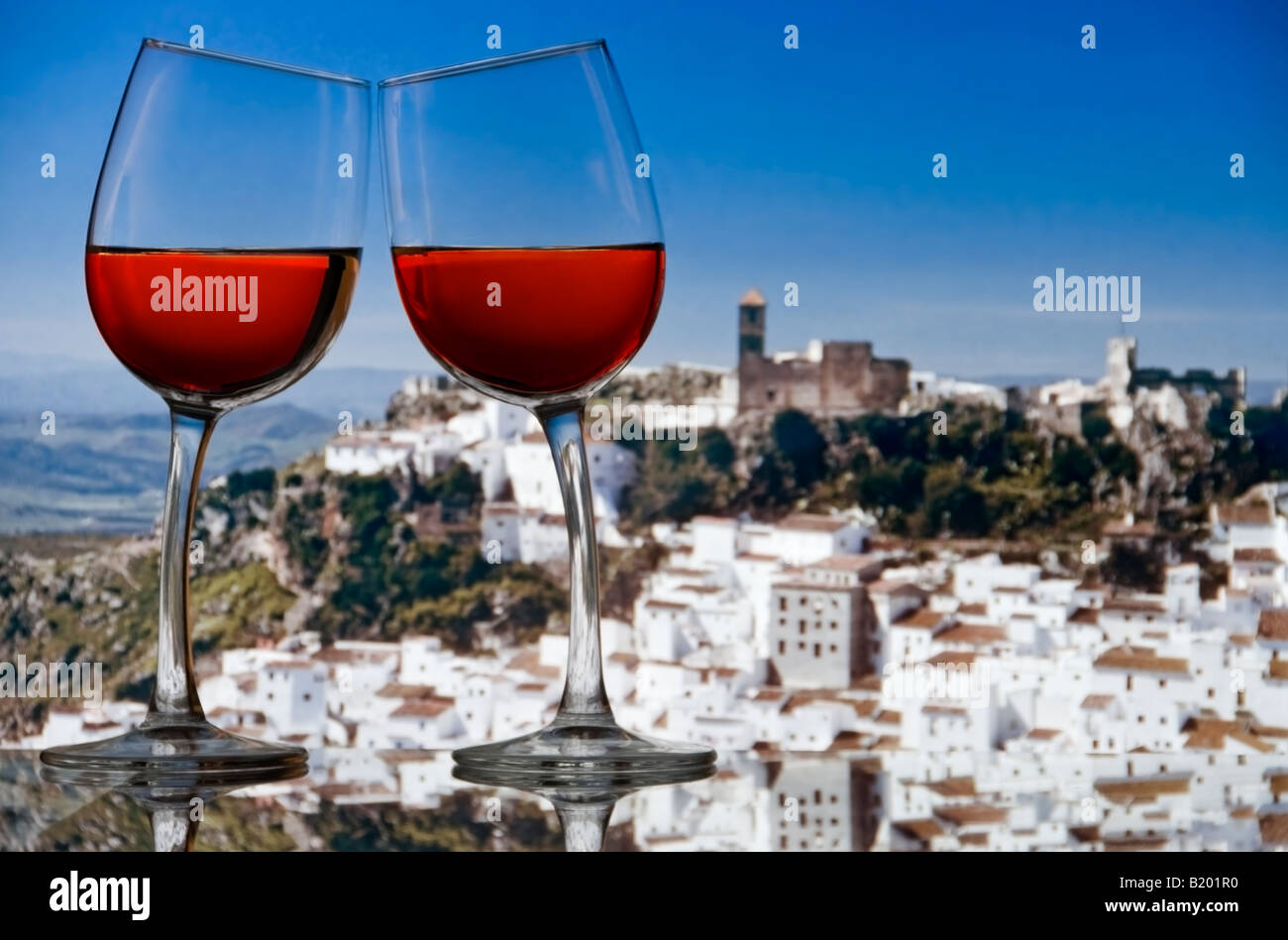 Due vini rosati bicchieri lean gli uni verso gli altri con bianco andaluso hilltop village di Casares in background Costa del Sol Spagna Foto Stock