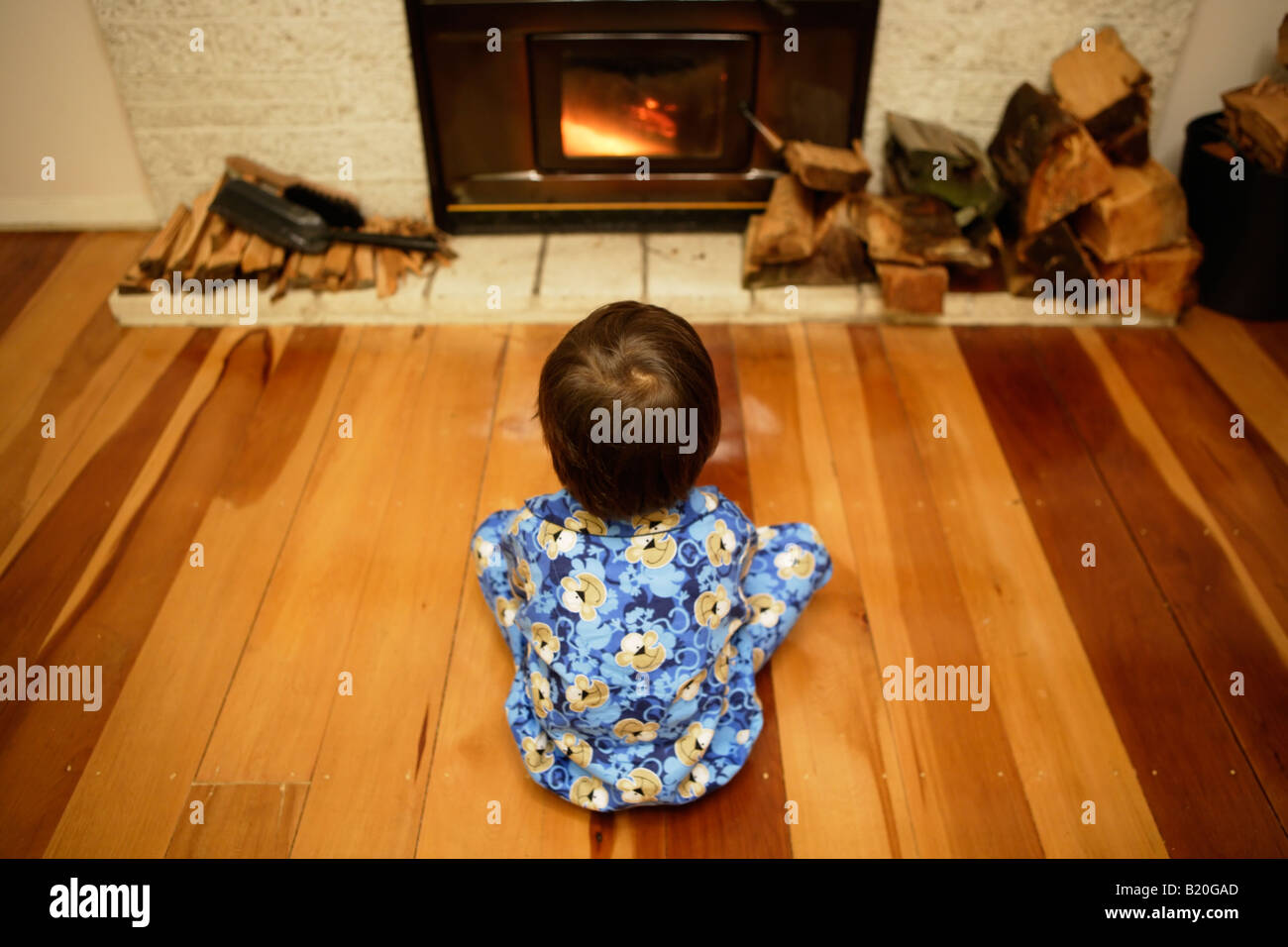 Ragazzo di età compresa tra i sei si siede di fronte a log un fuoco che brucia il legno è a zero emissioni di carbonio combustibile rinnovabile Foto Stock