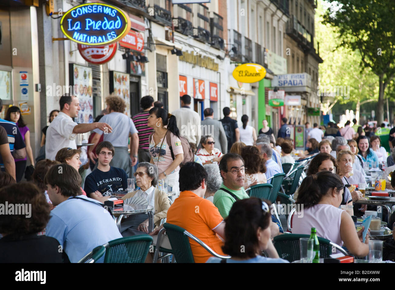 Spagna Madrid persone sedersi a affollata tavoli all'aperto lungo il Paseo del Prado street nel tardo pomeriggio ristoranti marciapiede in linea Foto Stock