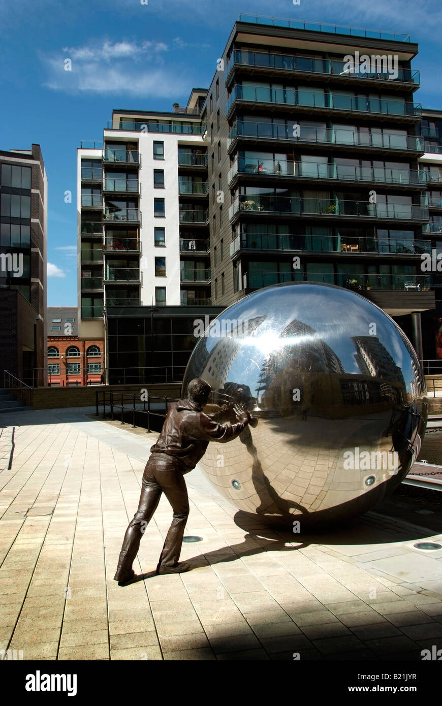 Una scultura di un lavoratore spinge una sfera a specchio sulla banchina di Clarence Dock con blocchi di appartamenti in aumento oltre Foto Stock