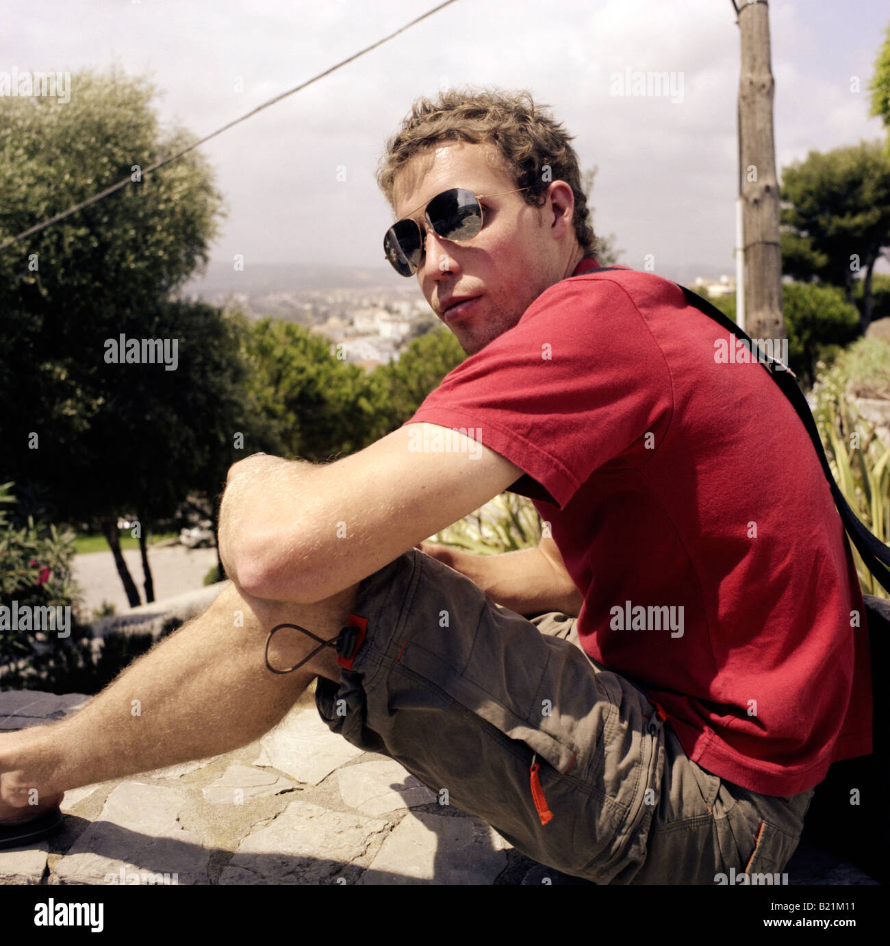 Anno Gap studente in pantaloncini corti e rosso tee shirt seduto su una parete che guarda verso la telecamera Foto Stock