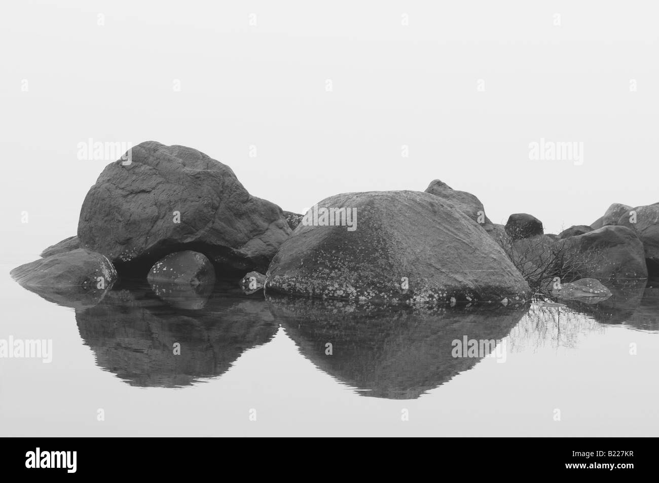 Rock riflettendo su ancora un lago mentre una fitta nebbia nasconde il resto dei dintorni. Foto Stock