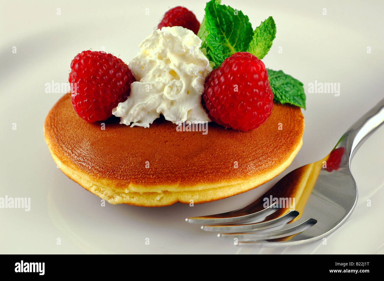 Lampone shortcake con menta fresca e panna montata su una piastra bianca con una forcella Foto Stock
