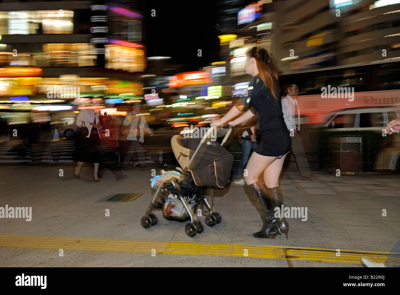 Donna Giapponese in mini gonna spingendo la PRAM sulle strade di Sendai di notte Sendai, Giappone Foto Stock