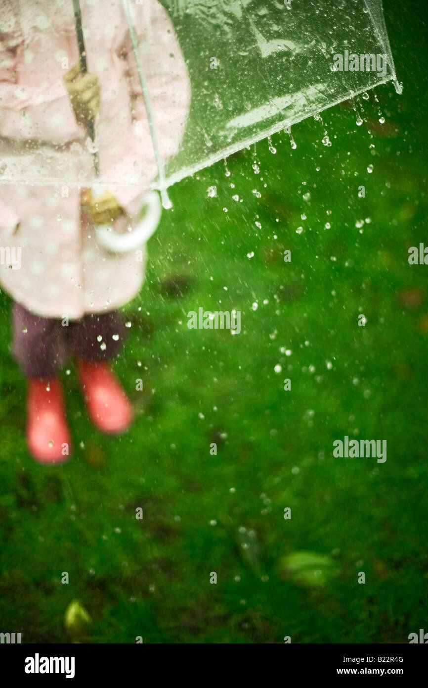 Bambina di cinque anni si trova in giardino con ombrellone in un giorno di pioggia Foto Stock