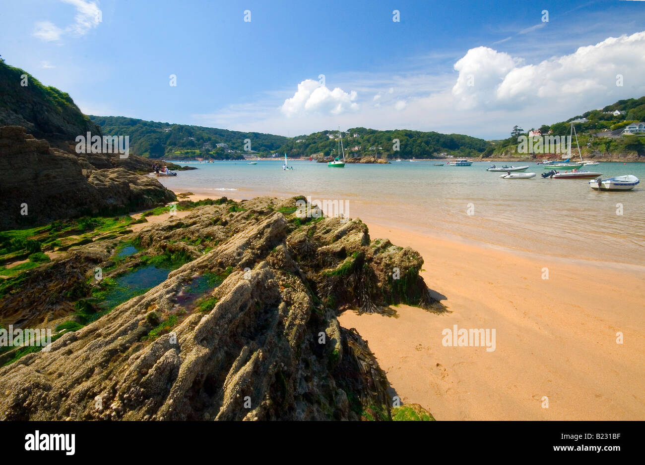 Una vista attraverso l'estuario di Salcombe da Sunny Cove Beach. Le rocce in primo piano, barche in background. Foto Stock