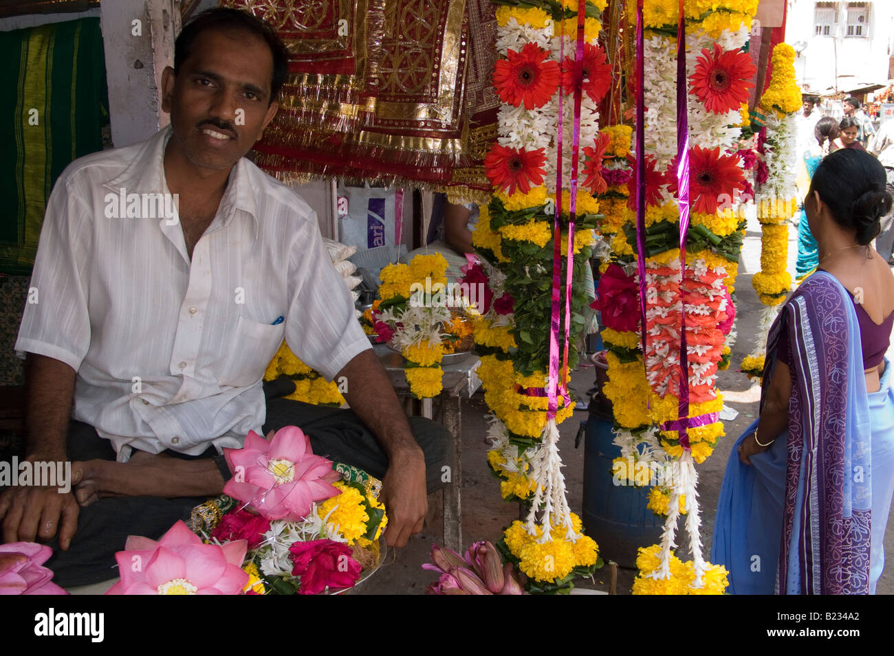 Uomo seduto in una bancarella di strada vendita di ghirlande di fiori come tempio offerte, Mahalaxmi West, Mumbai, India Maharashtra Foto Stock