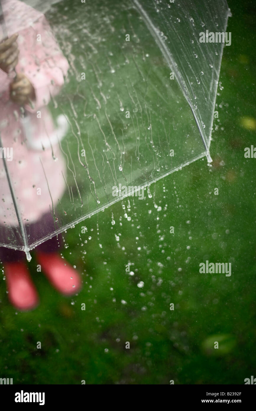 Bambina di cinque anni si trova in giardino con ombrellone in un giorno di pioggia Foto Stock