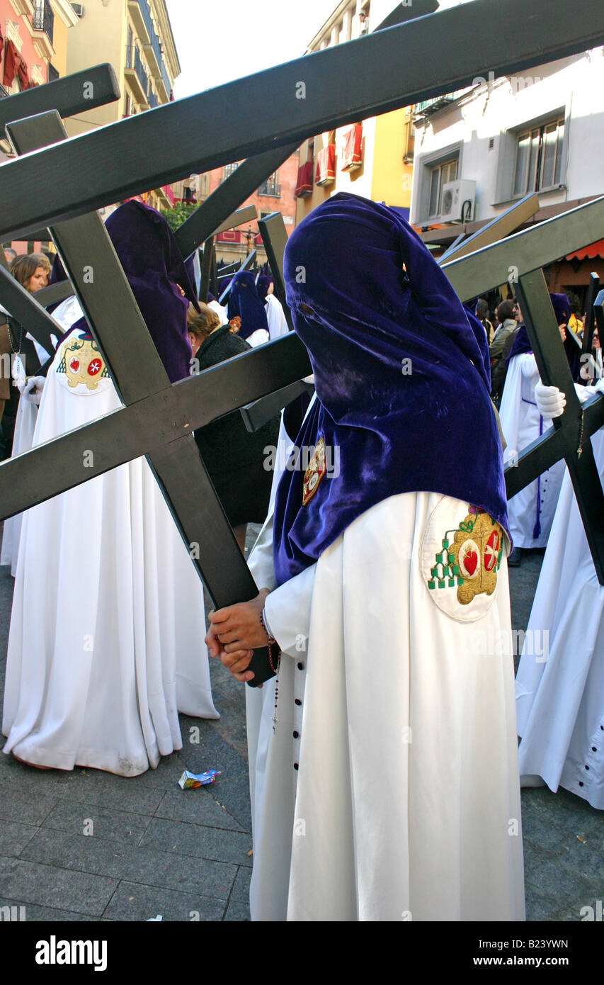 Penitente in viola il cofano e vesti bianche che porta una croce, semana santa, Siviglia, Spagna Foto Stock
