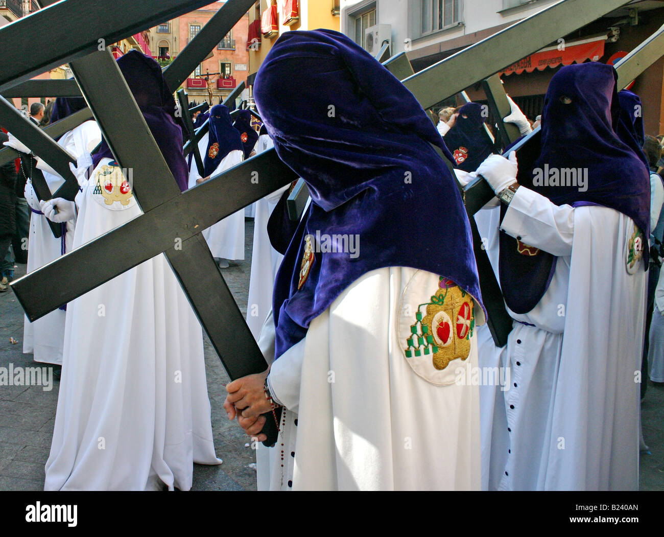 Penitente in viola il cofano e vesti bianche che porta una croce, semana santa, Siviglia, Spagna Foto Stock