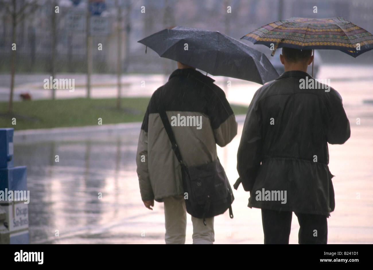 Coppia caucasica a piedi sotto la pioggia con ombrelloni Foto Stock