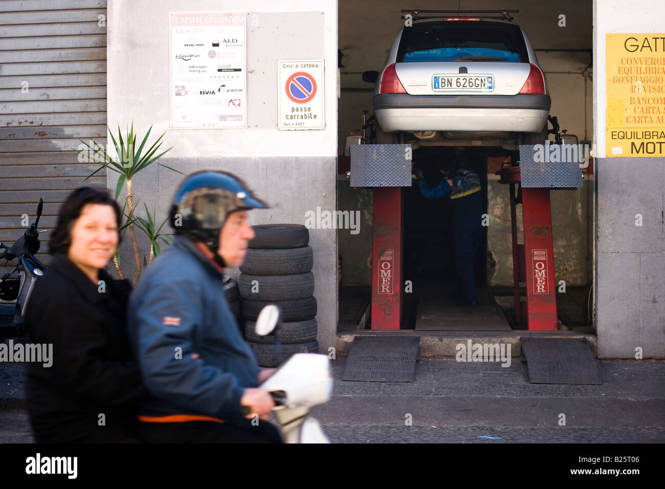 Anziana coppia siciliana cavalca una moto passato un garage in Catania, Sicilia, Italia Foto Stock