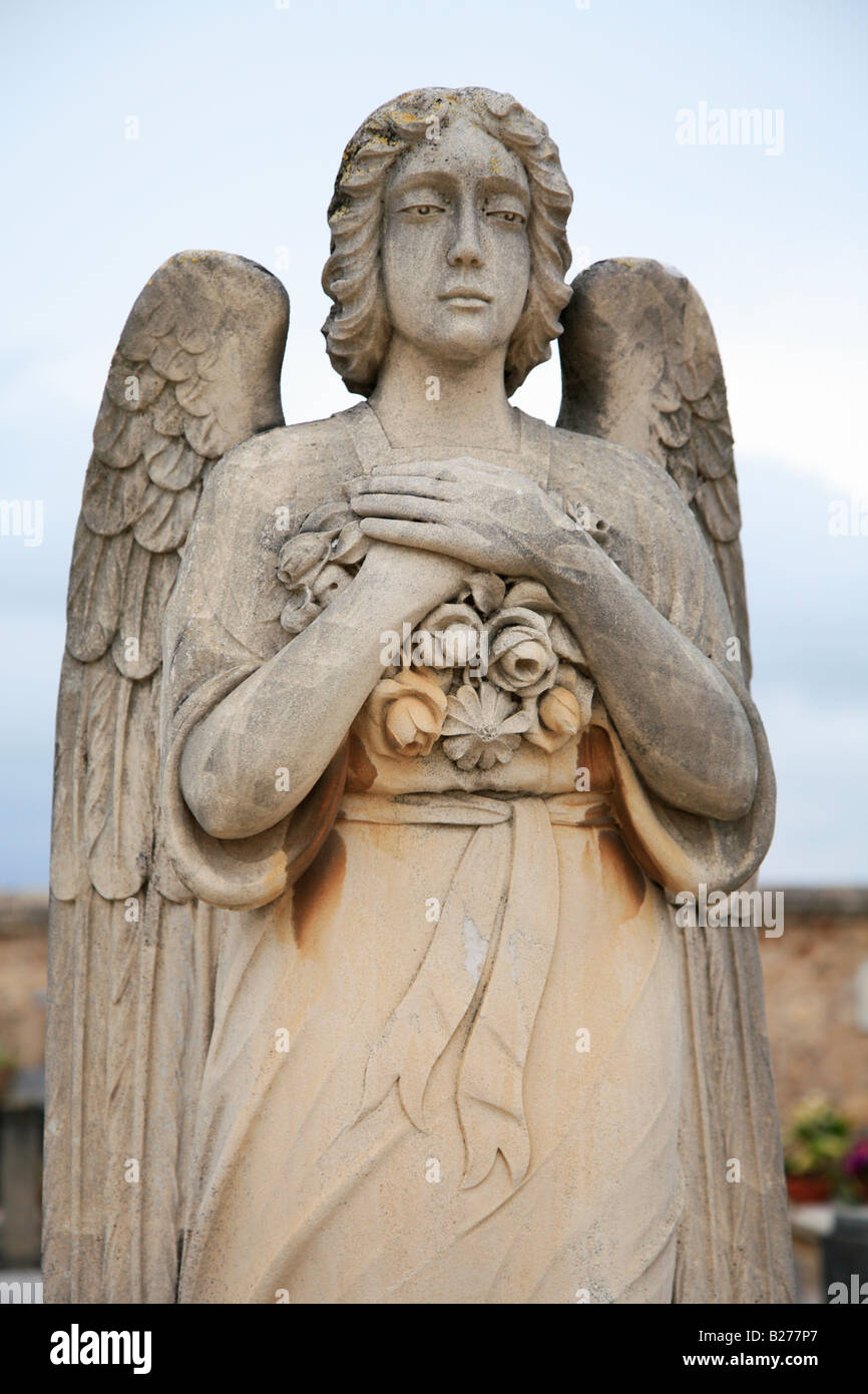 Statua di un angelo femmina fatta di colore arancio pietra l'angelo tiene in mano un mazzo di fiori contro il suo torace. Foto Stock