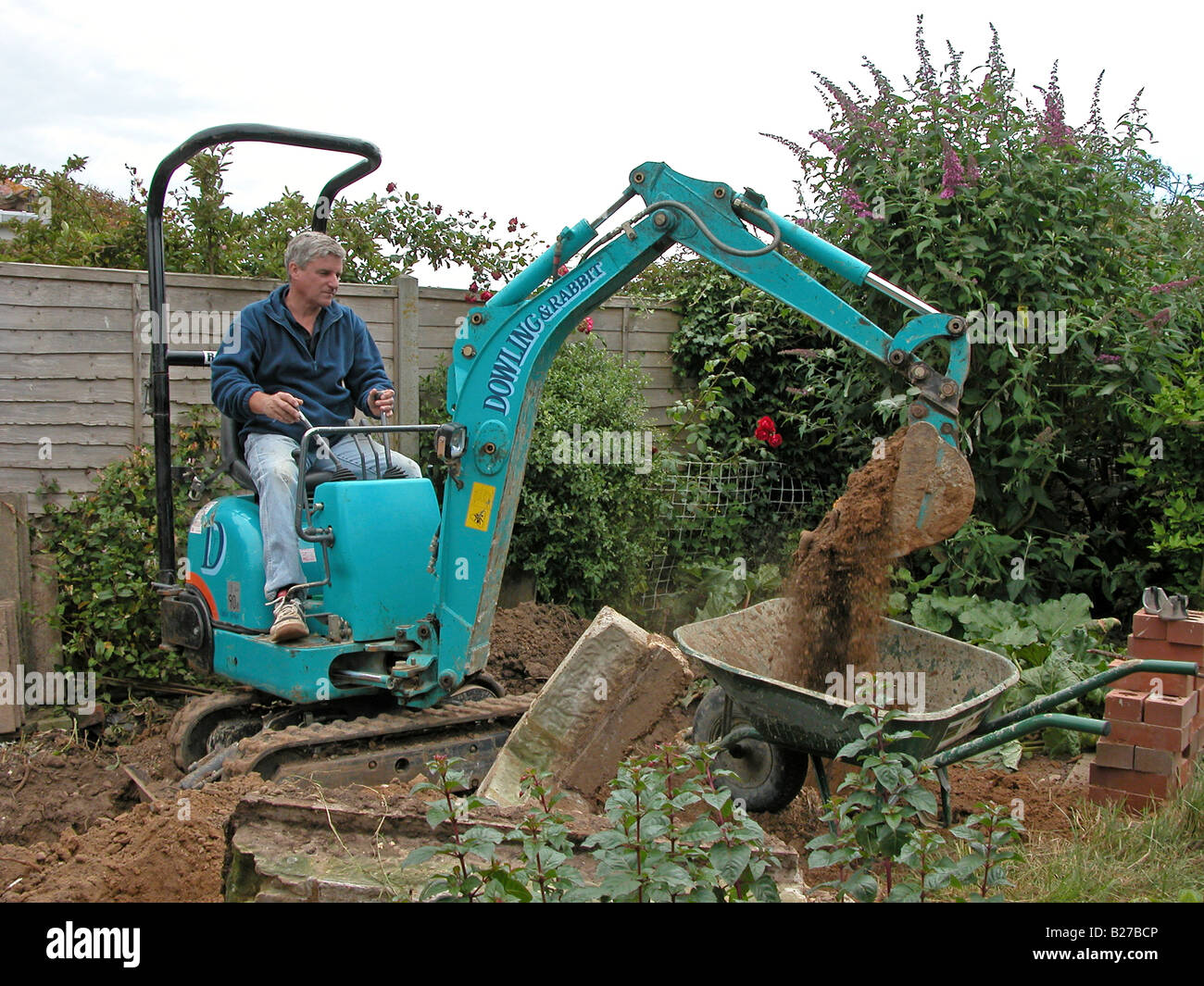 Builder / lavoratore edile utilizzando un Dowling & Coniglio escavatore mini escavatore a rimuovere il suolo prima di lavorare su un interno Foto Stock