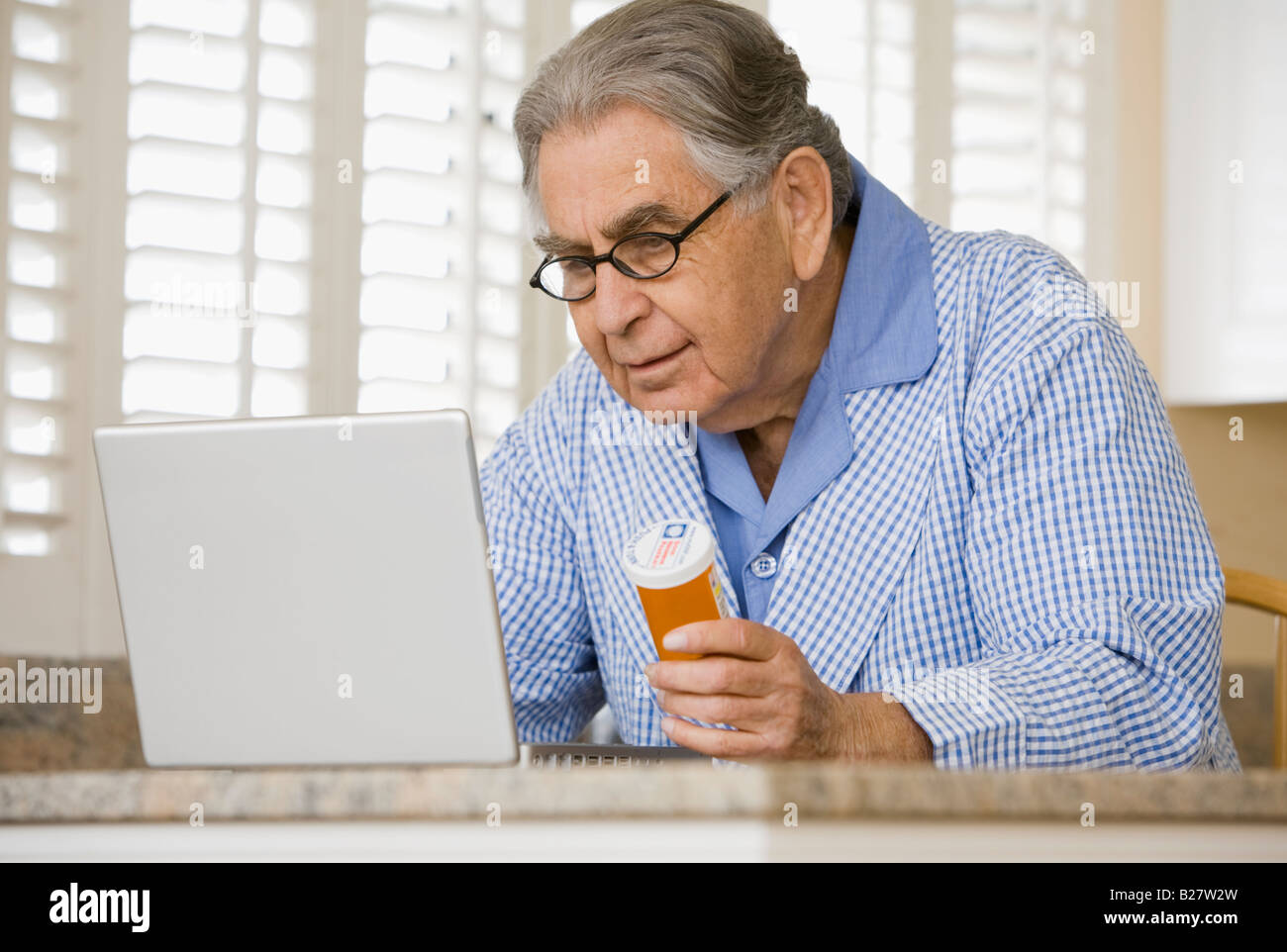 L'uomo anziano con il flacone di farmaco guardando al laptop Foto Stock